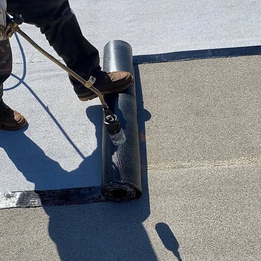 Roofer torch-applying modified bitumen membrane during a flat roof replacement